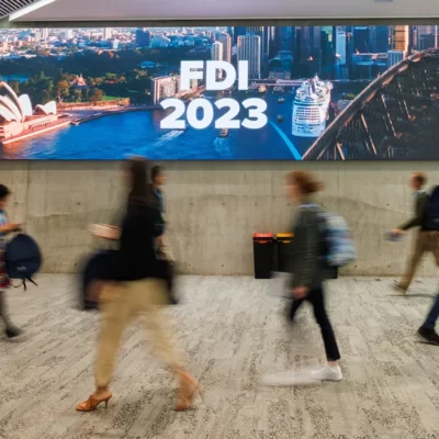 People walking past a sign with FDI 2023 on the screen